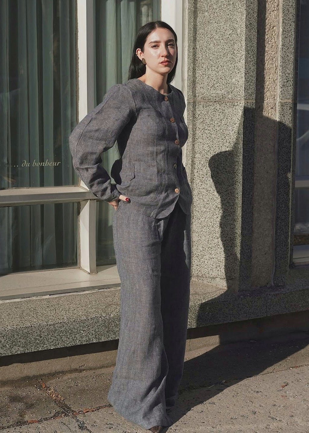 Woman in a gray suit standing against a building with a shadow.