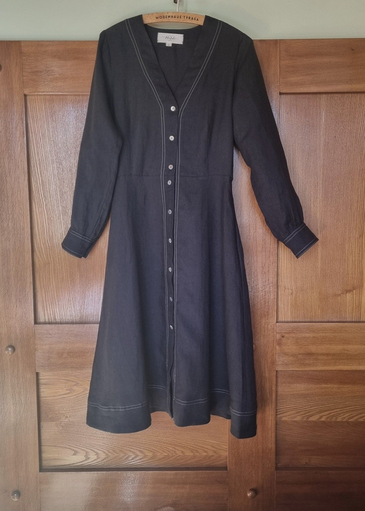 Black dress with white buttons on a wooden door