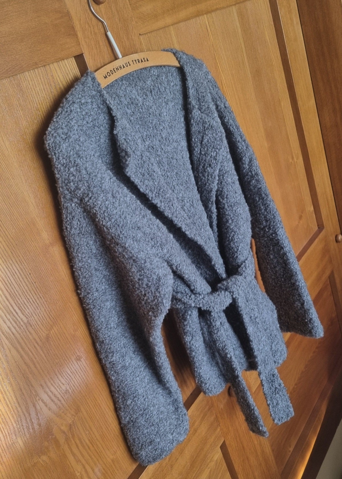 Gray fuzzy cardigan on a wooden hanger against a wooden door background