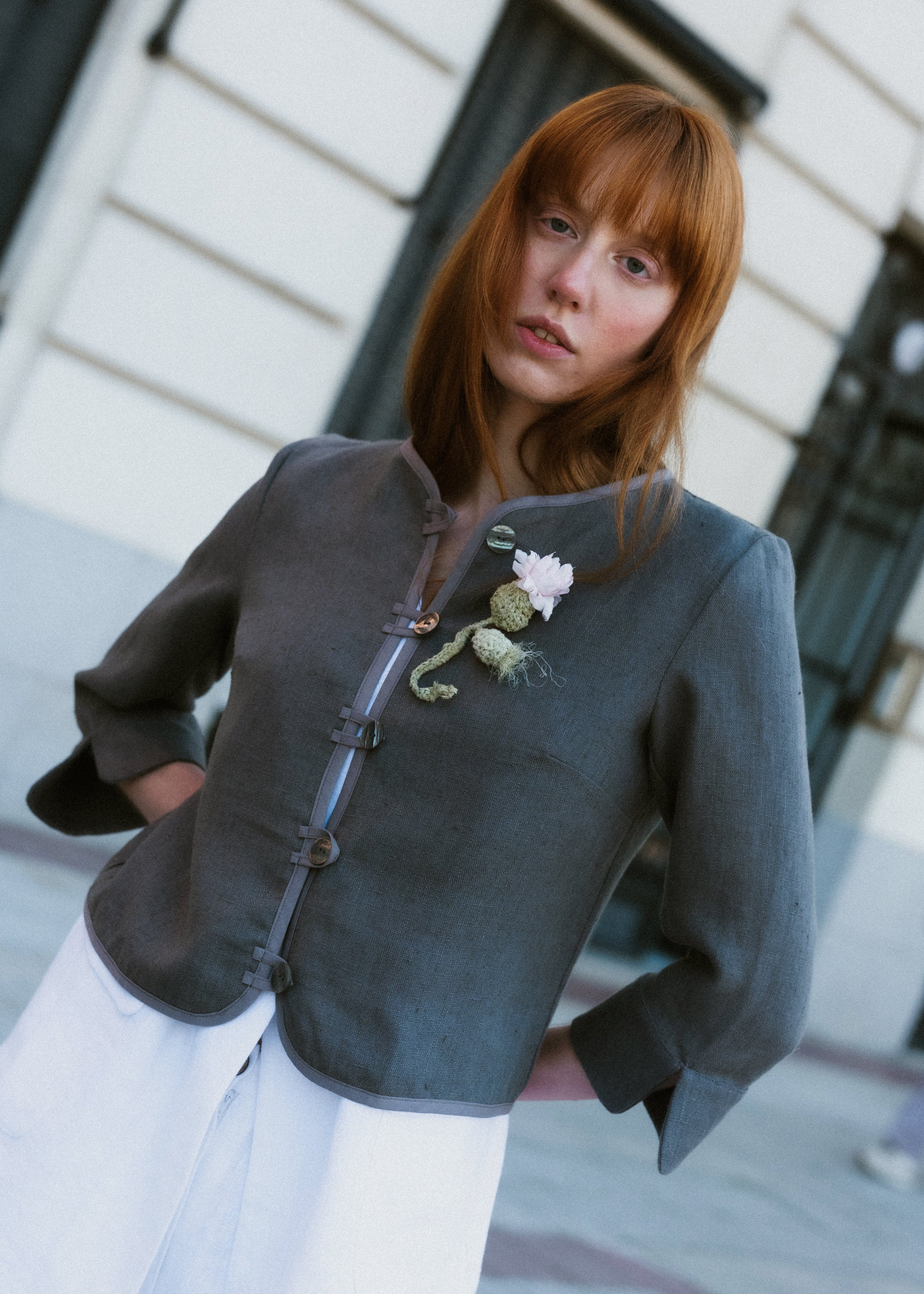 Woman wearing a dark gray jacket with floral details, standing outdoors.