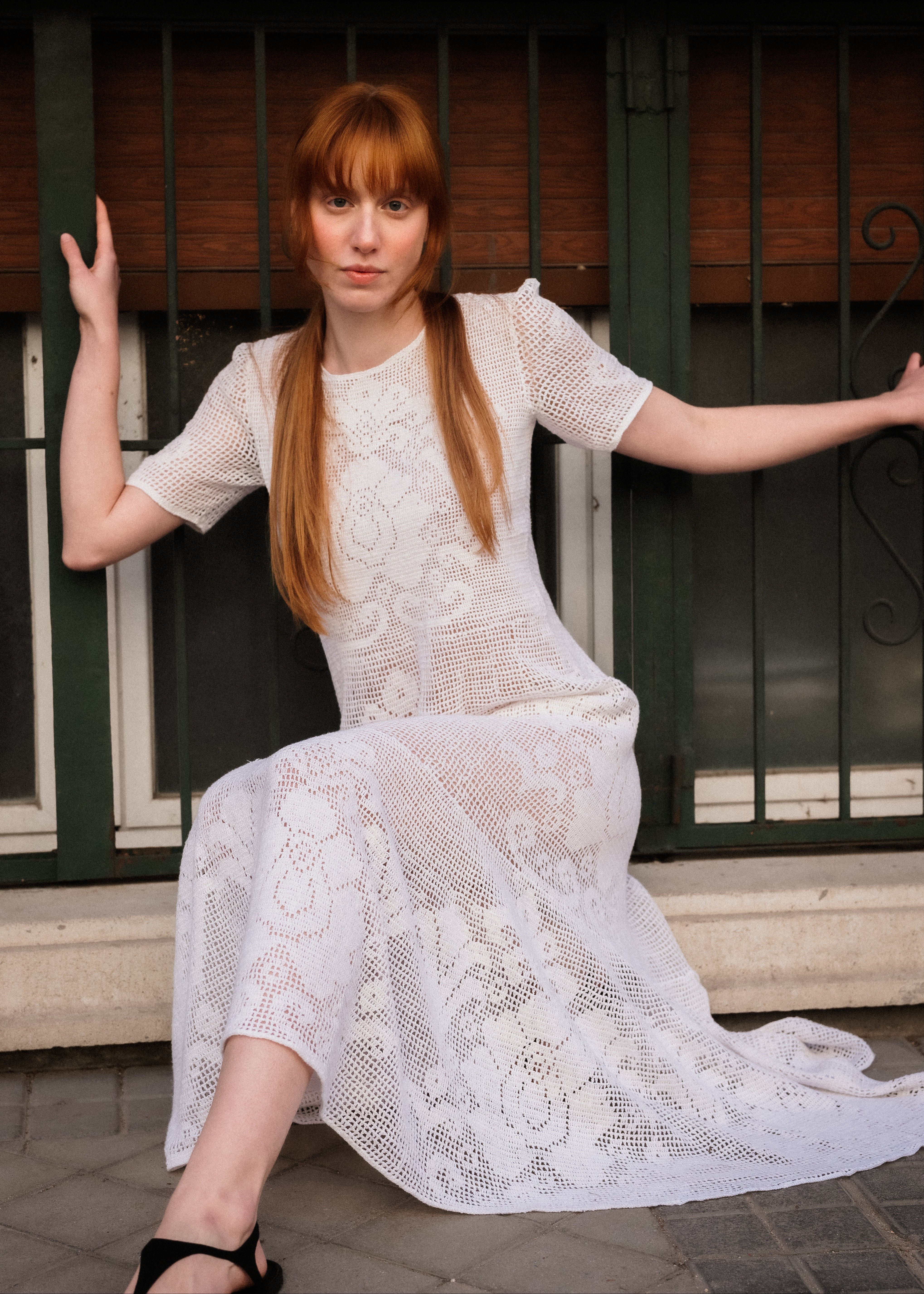 Woman in a white lace dress sitting on a step with a metal gate in the background