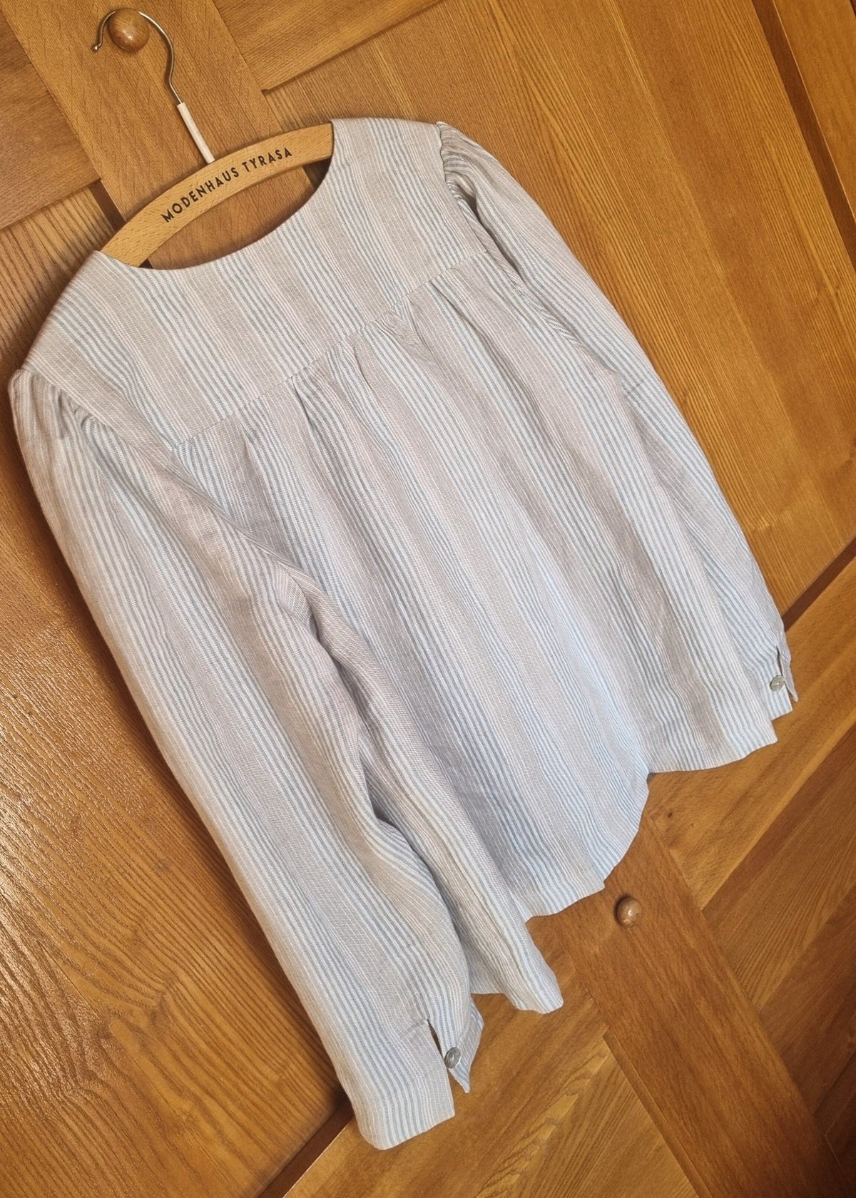 Light-colored blouse on a wooden hanger against a wooden floor background