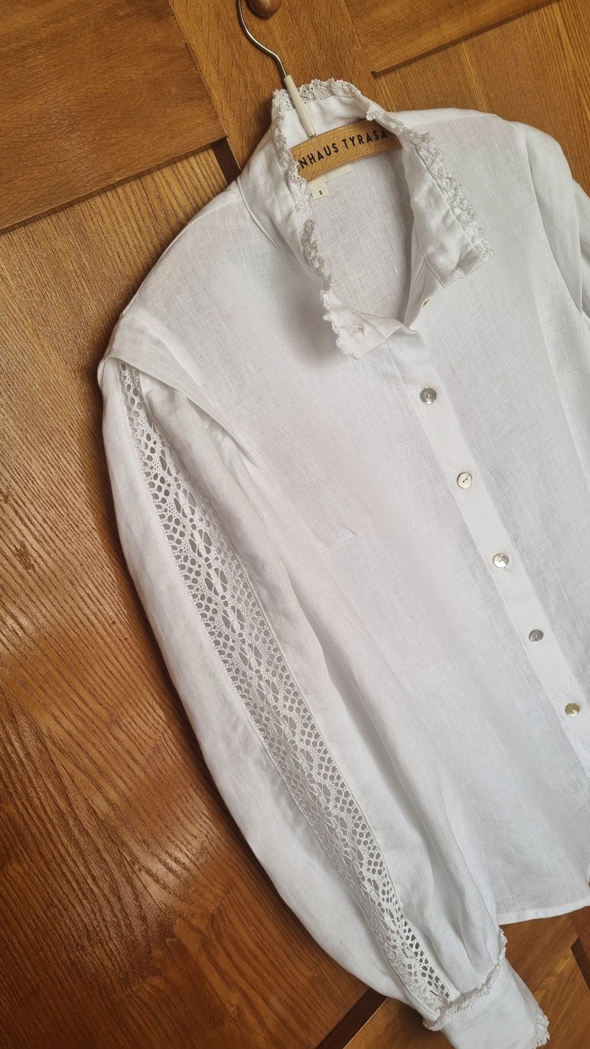 White lace-trimmed blouse on a wooden hanger against a wooden floor background