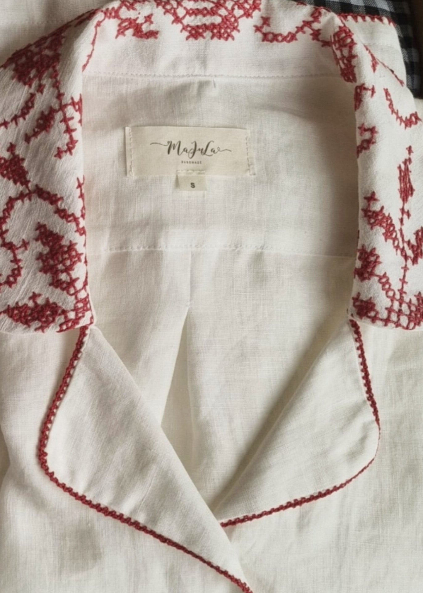 White garment with red embroidery and a brand label on a blurred background