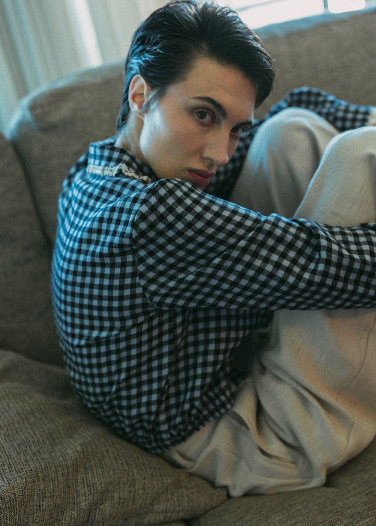 Person wearing a checkered shirt and light pants sitting on a couch.