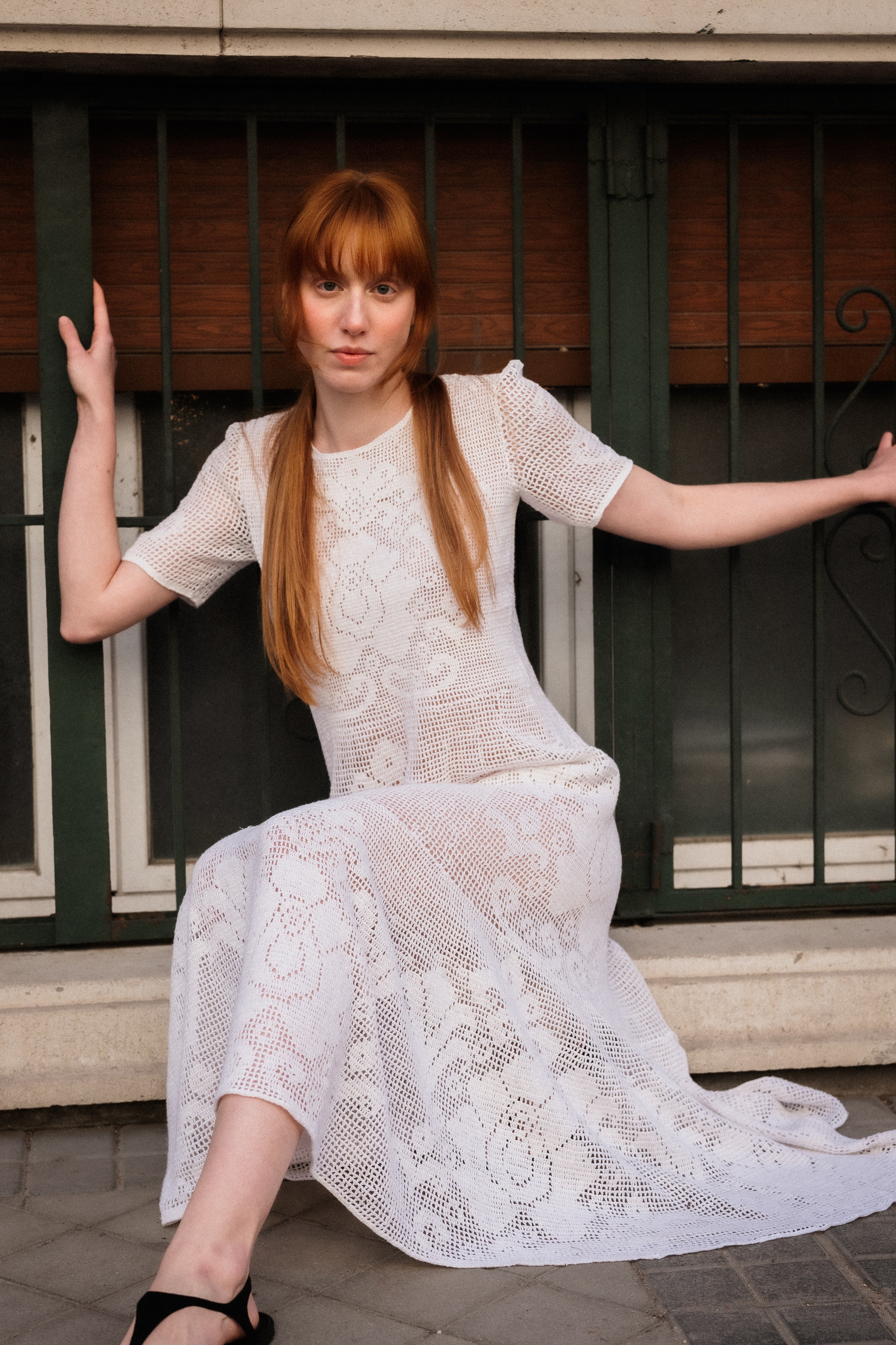 Woman in a white lace dress sitting on a step with a metal gate in the background