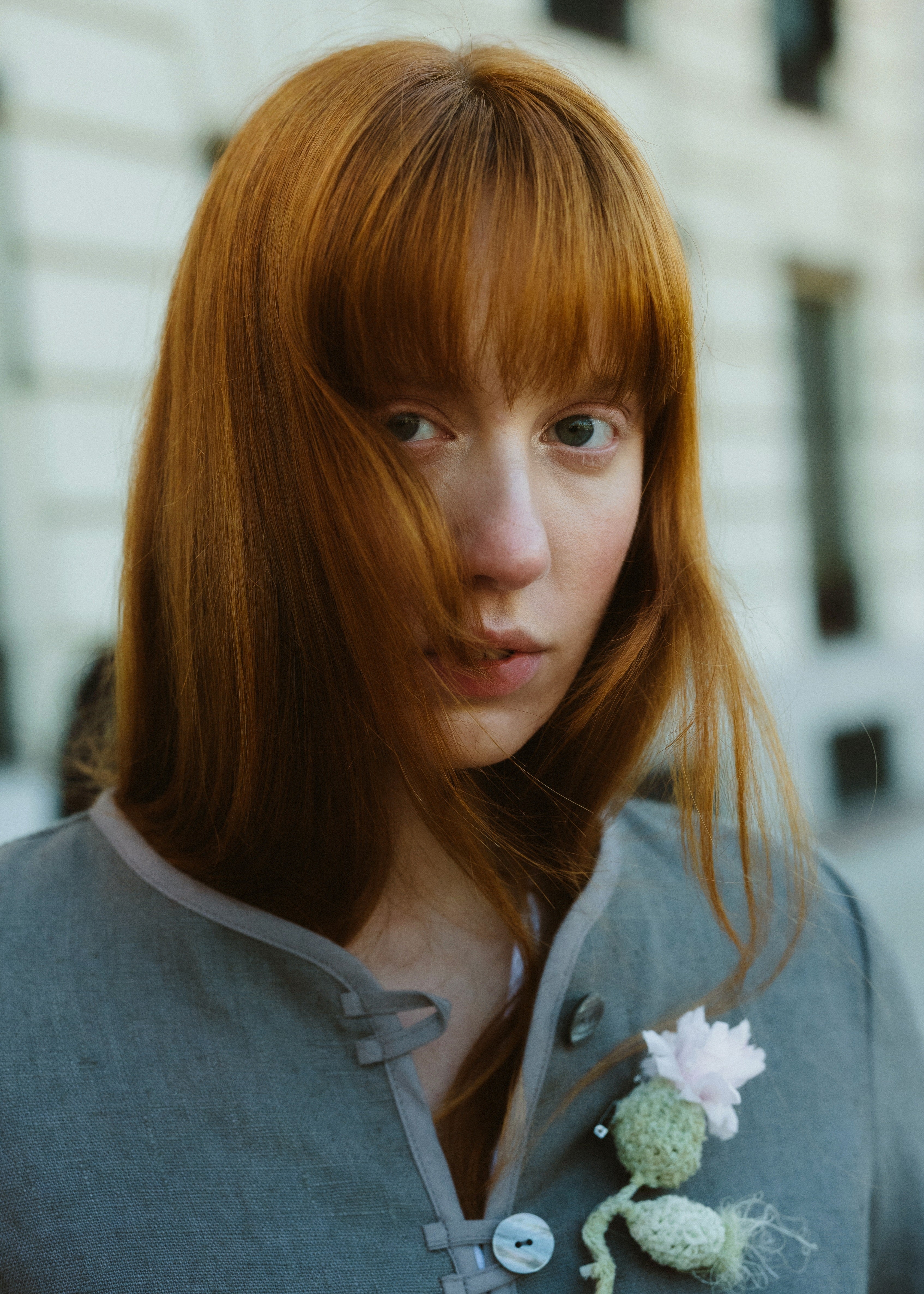 Person with red hair wearing a gray sweater with a floral brooch.