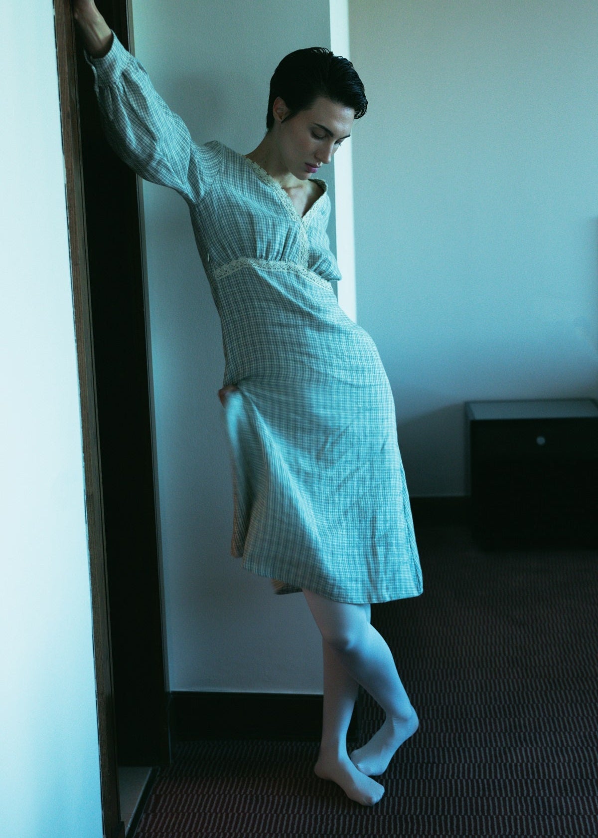 Person wearing a light blue robe standing in a room with a white wall.