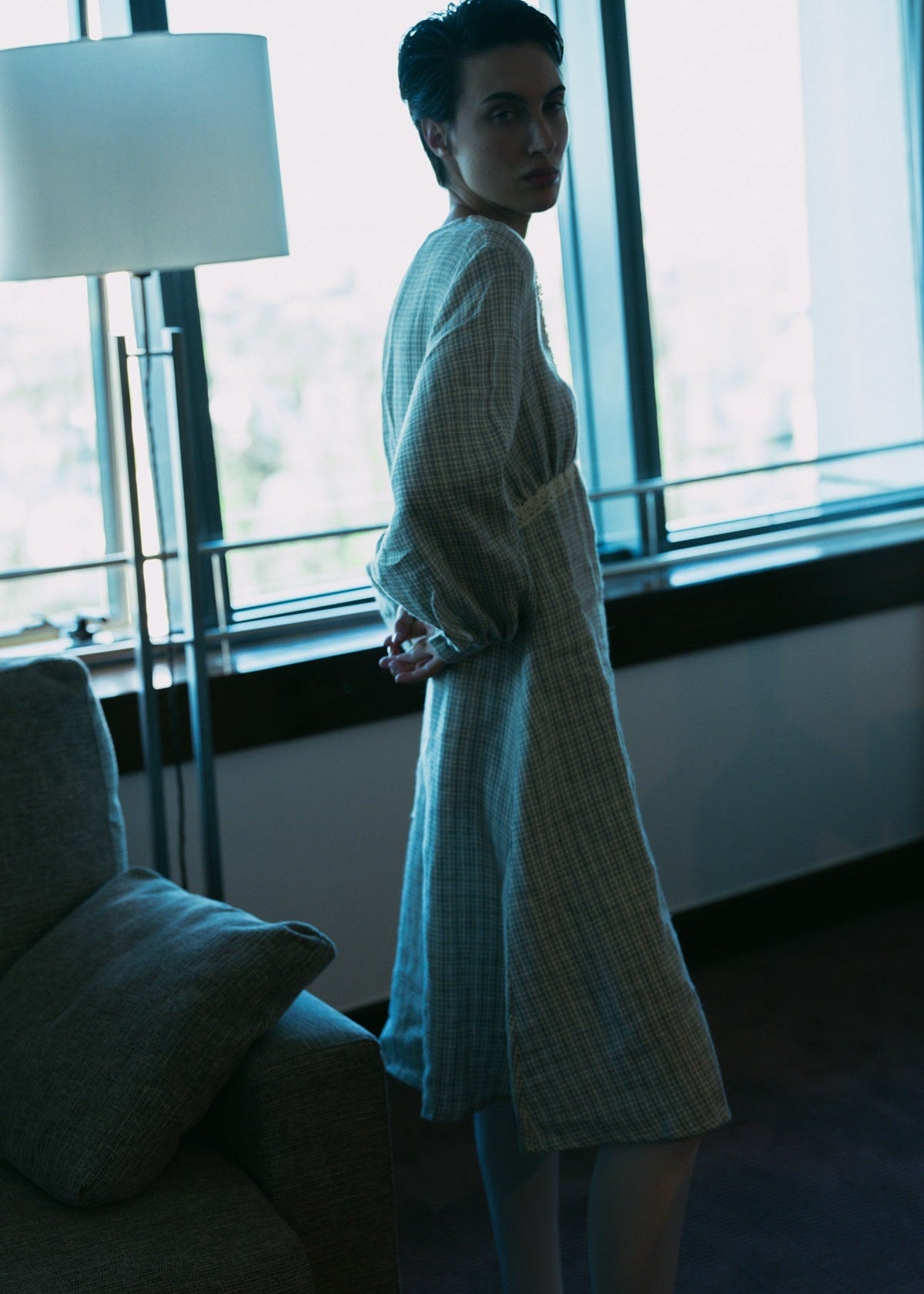 Person wearing a light blue robe standing in a room with large windows.