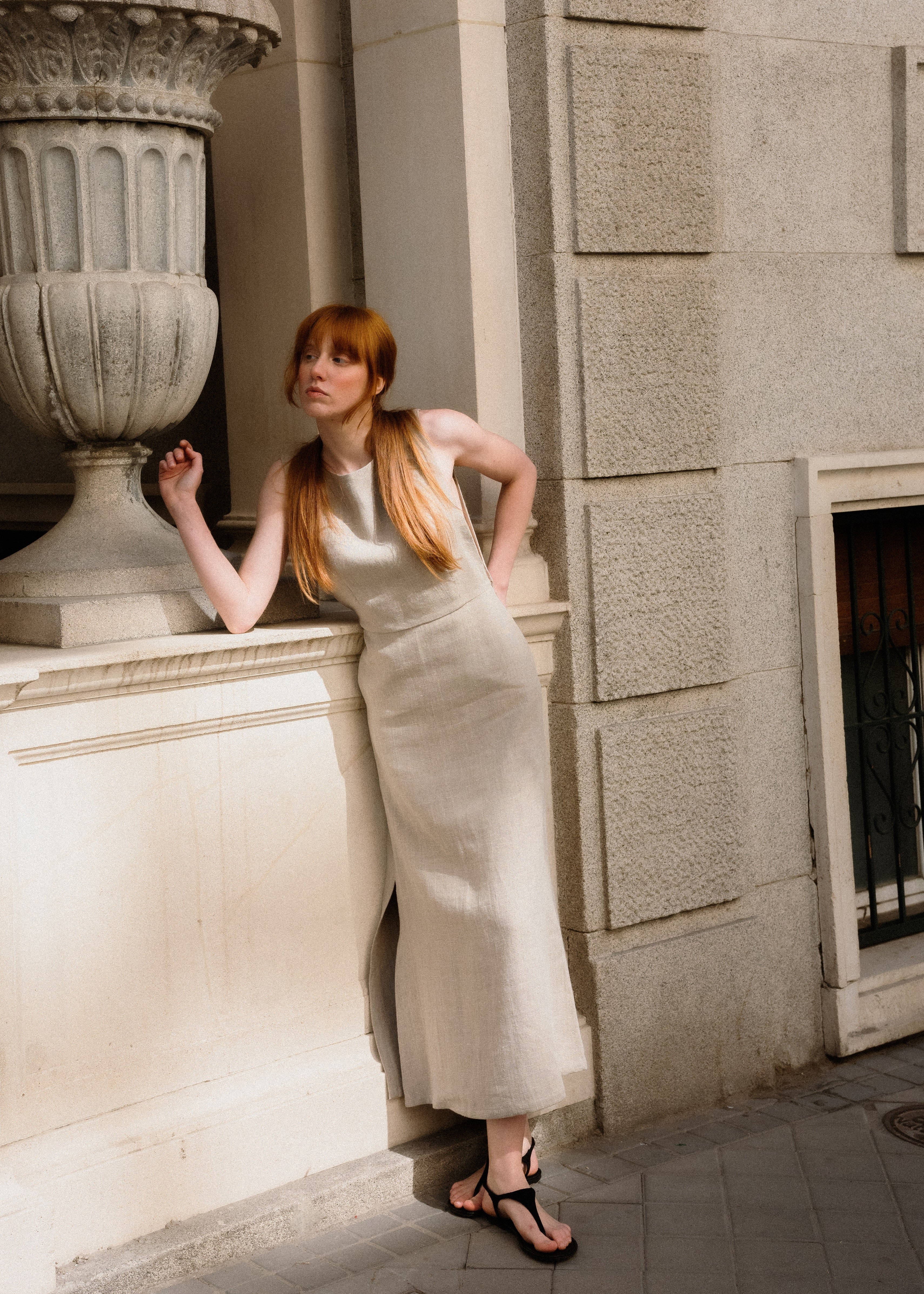 Woman in a white dress leaning against a stone wall with a large decorative urn.