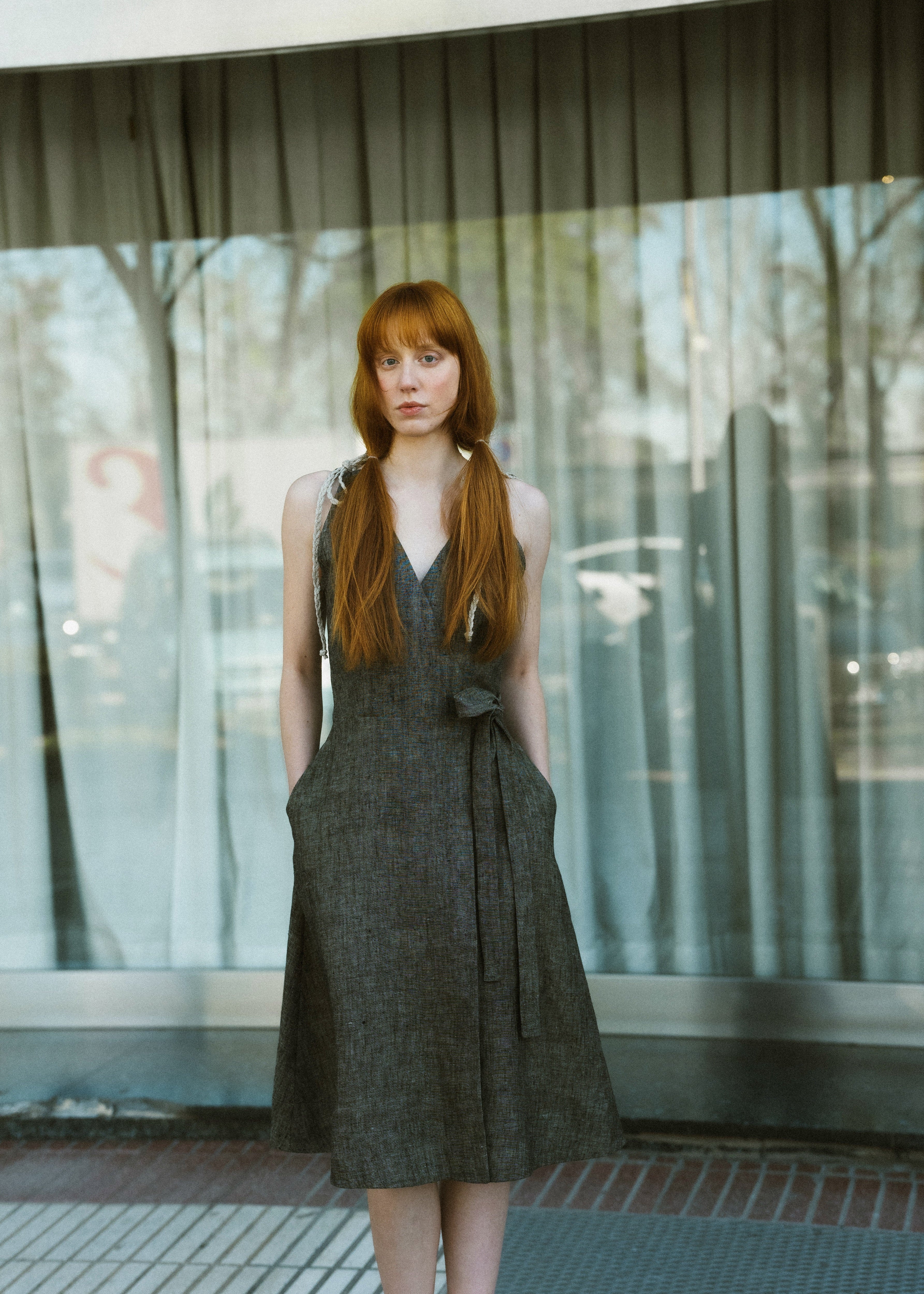 Woman in a dark green dress standing in front of a glass wall with reflections.