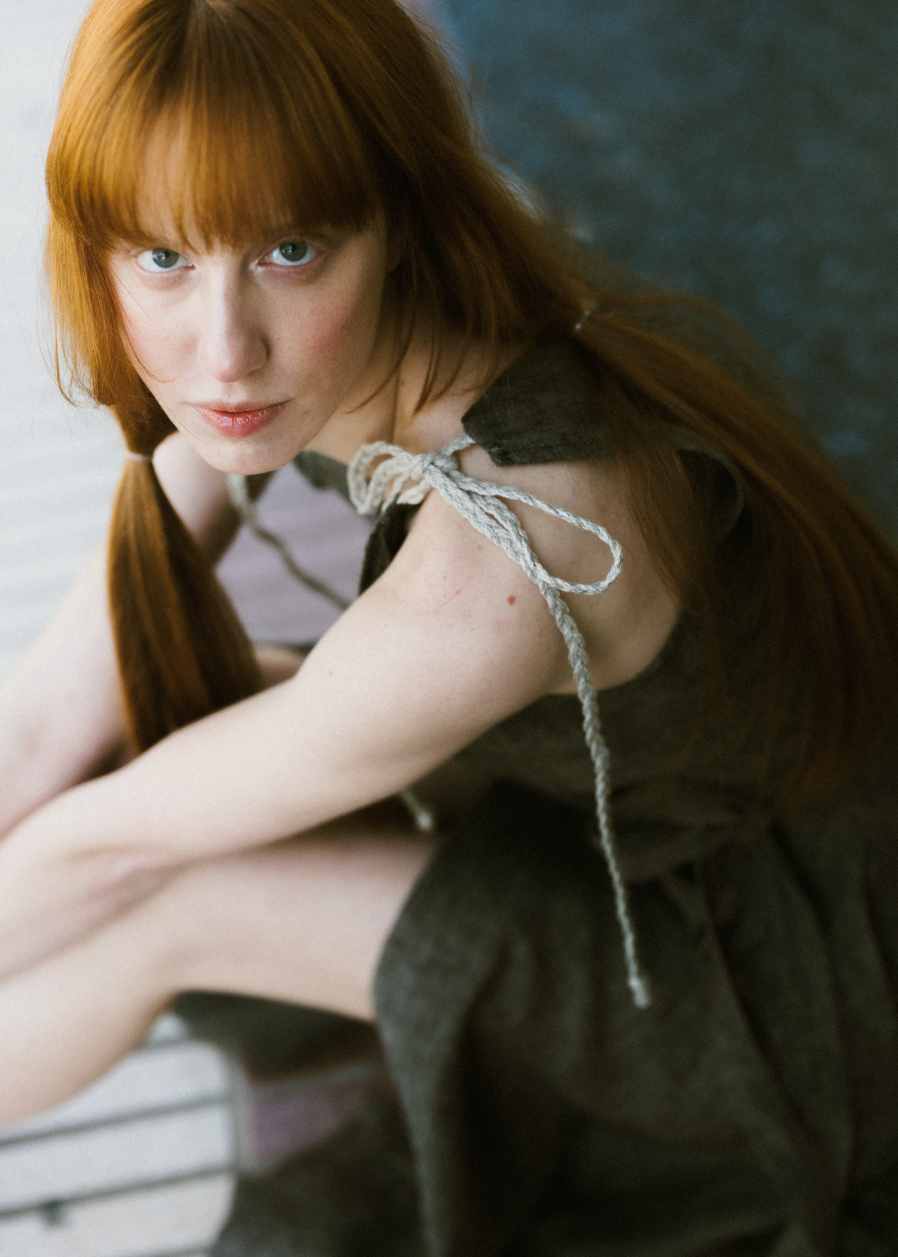 Woman with red hair wearing a dark green dress against a textured wall.