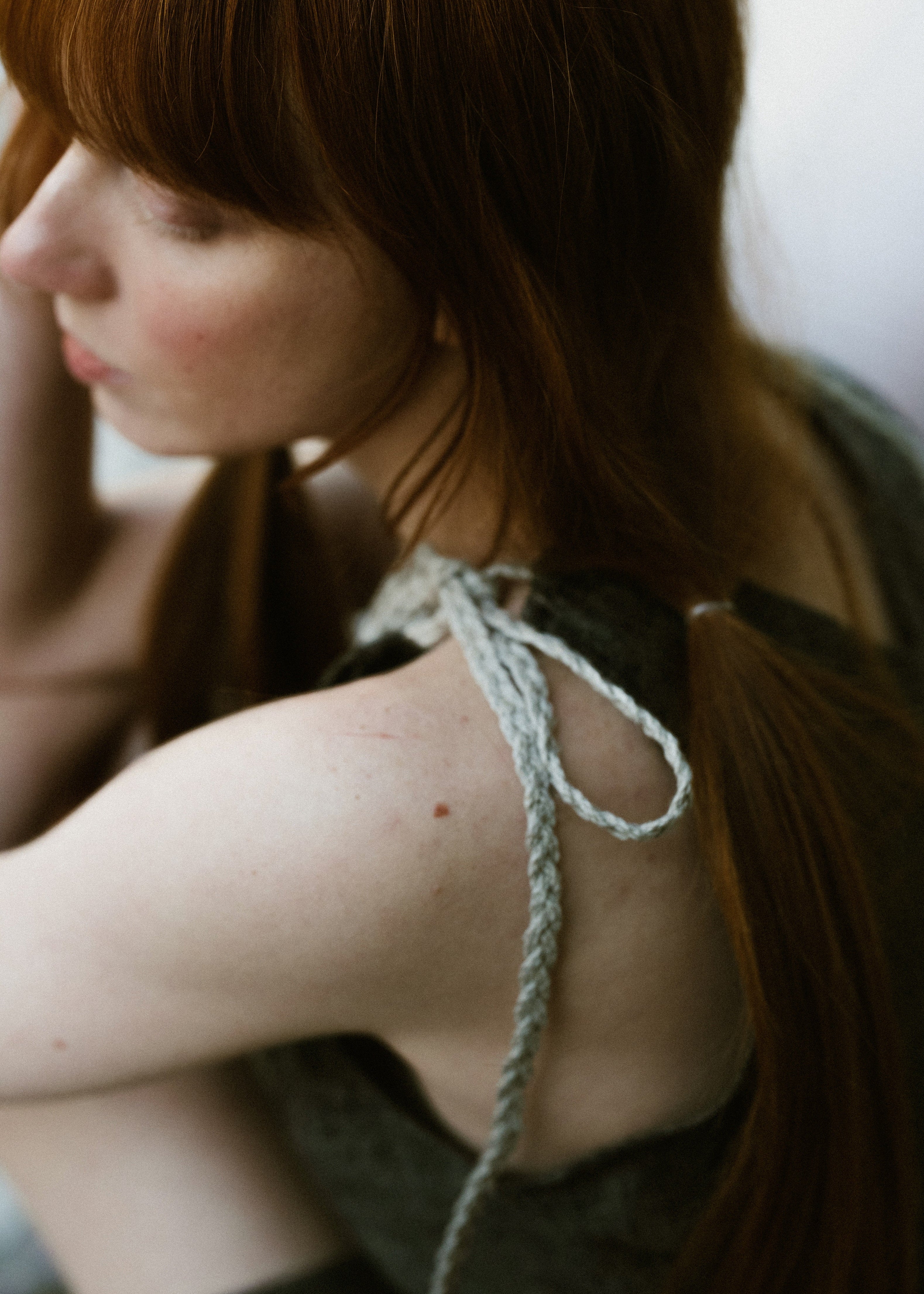 Woman with red hair wearing a green dress with a string detail on a blurred background