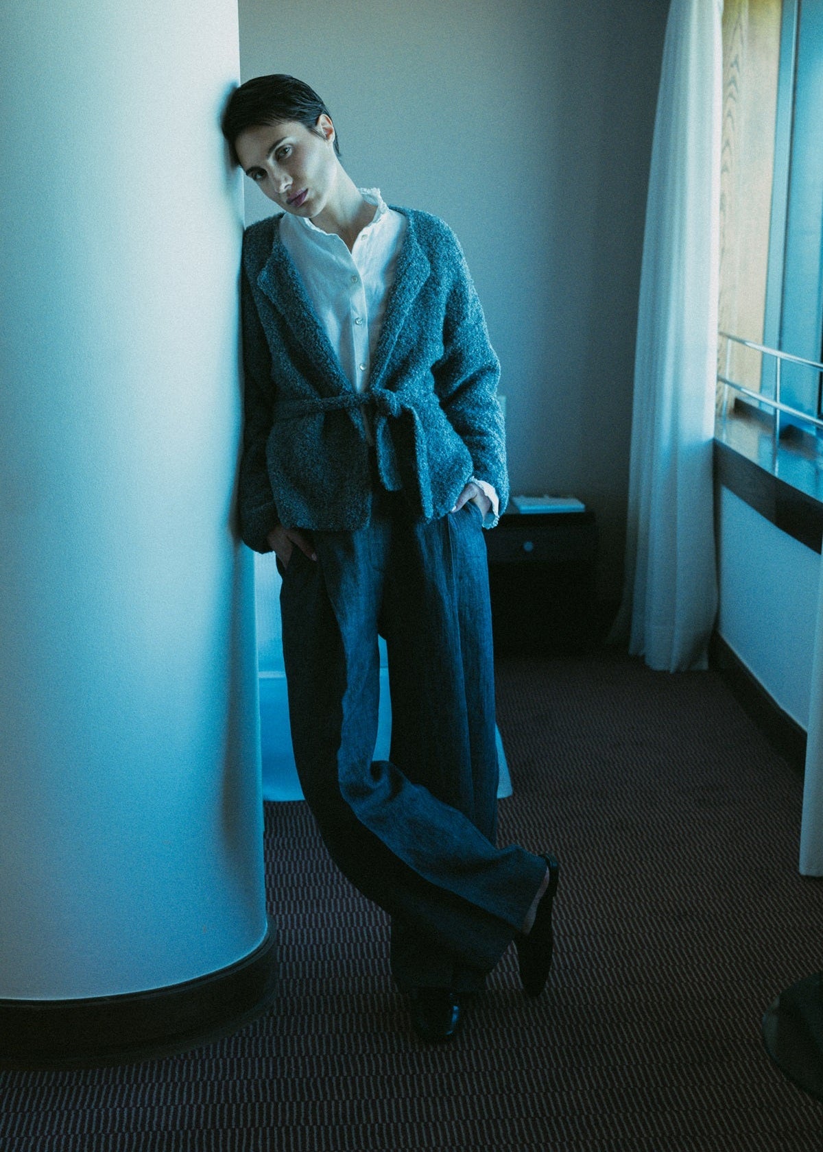 Person wearing a teal robe in a room with a window and curtain.