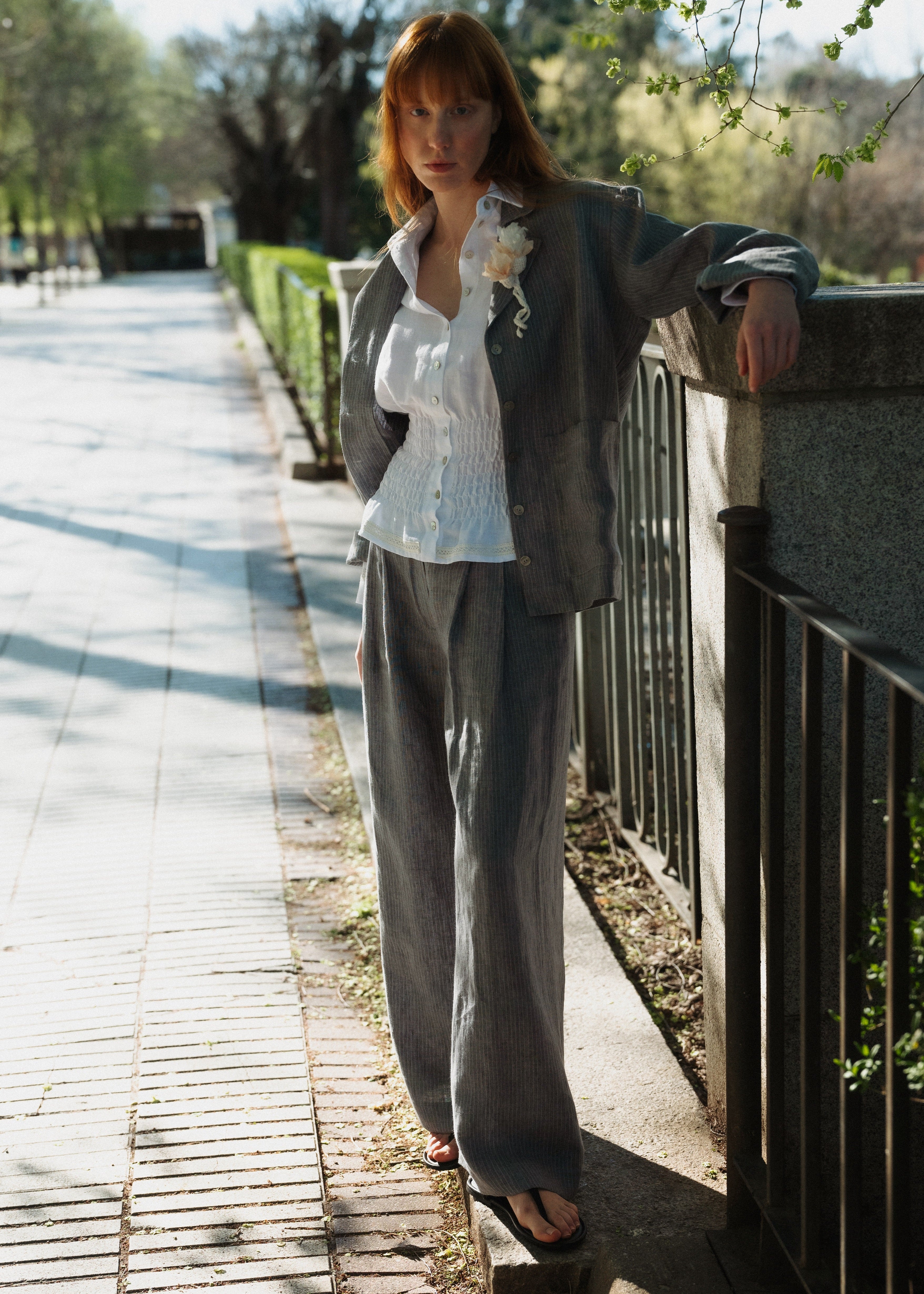 Woman standing on a sidewalk with a cat on her shoulder, leaning against a railing.