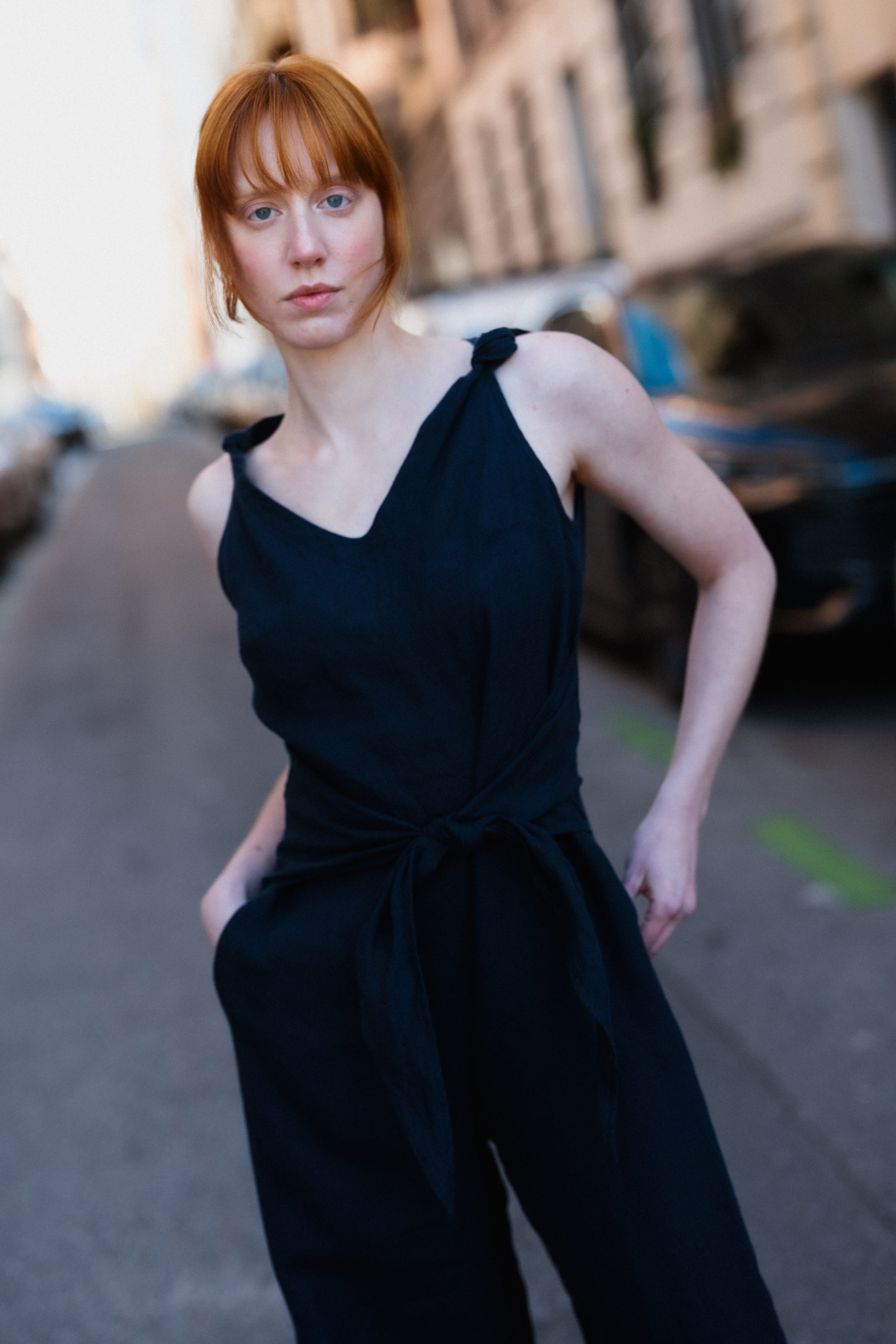 Woman in a black sleeveless jumpsuit standing on a city street.