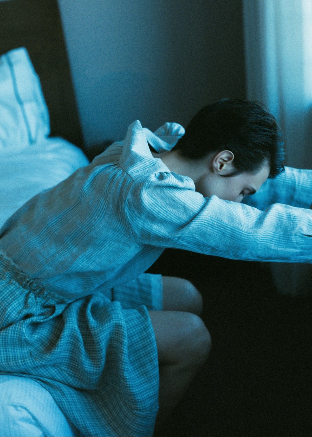 Person in a blue robe sitting on a bed in a dimly lit room