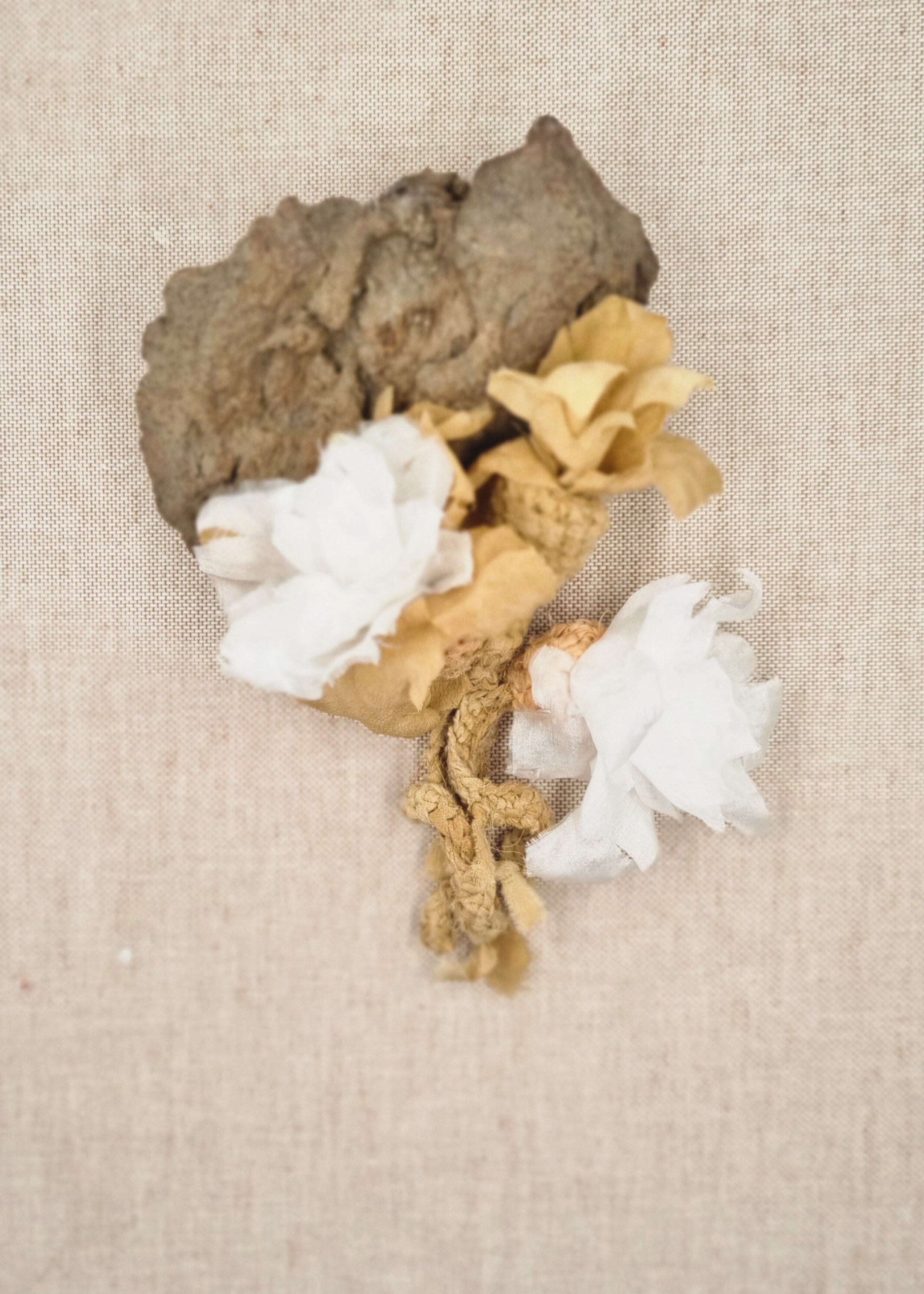 Decorative piece with gold leaf, white flowers, and gray stone on a beige fabric background