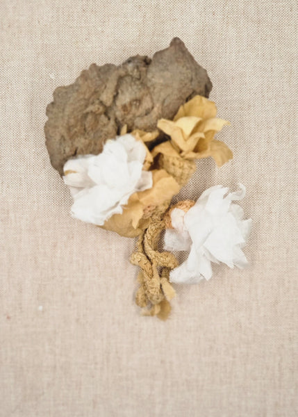 Decorative piece with gold leaf, white flowers, and gray stone on a beige fabric background