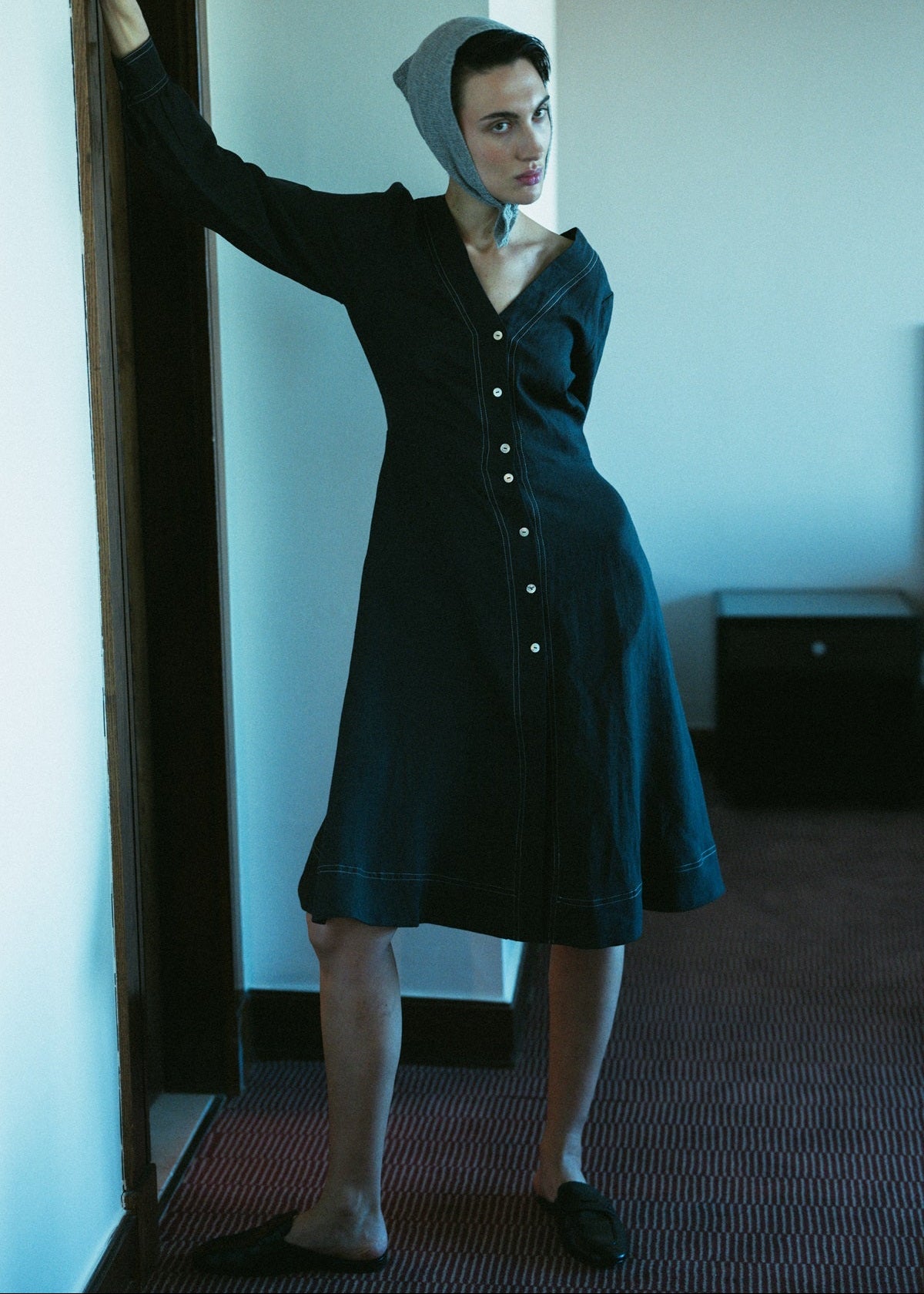 Woman in a dark dress and bonnet standing in a room with a mirror.