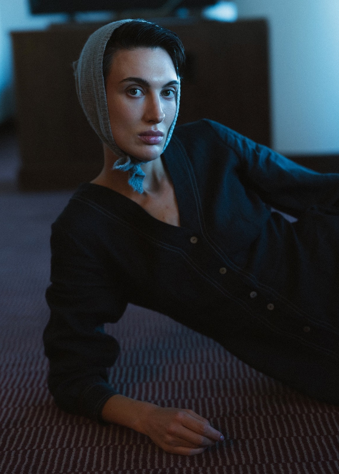 Person wearing a black outfit and headscarf in a dimly lit room