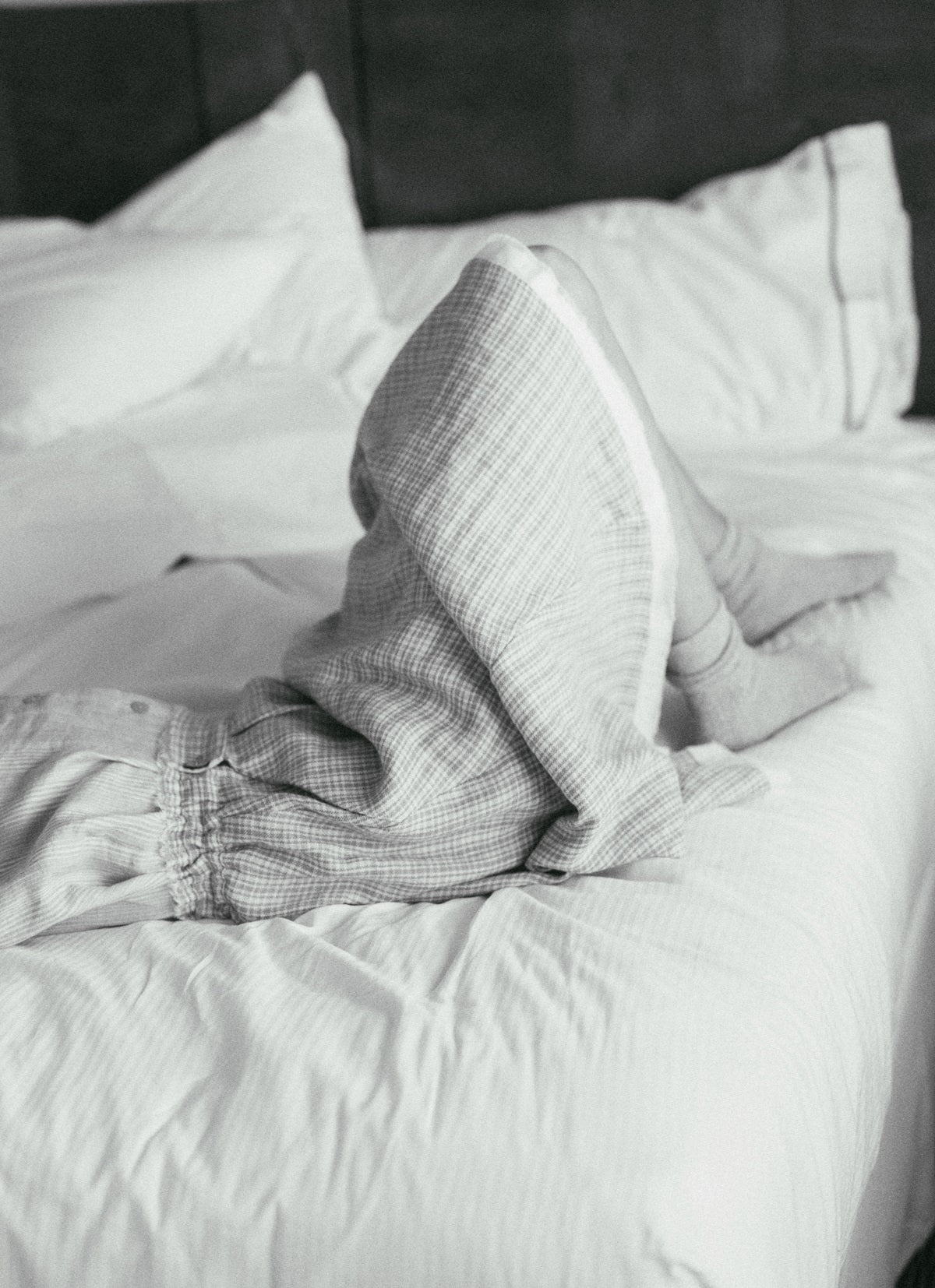 Person lying in bed with plaid pajama pants and a pillow, black and white photo