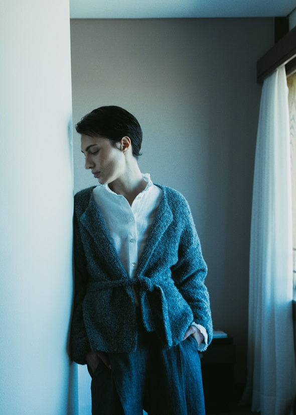 Person wearing a blue robe standing by a window in a room with neutral walls.