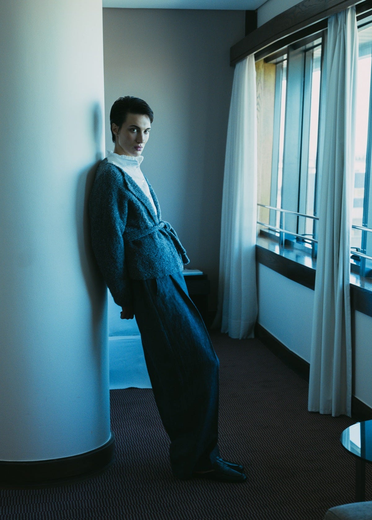 Person standing in a room with large windows and curtains