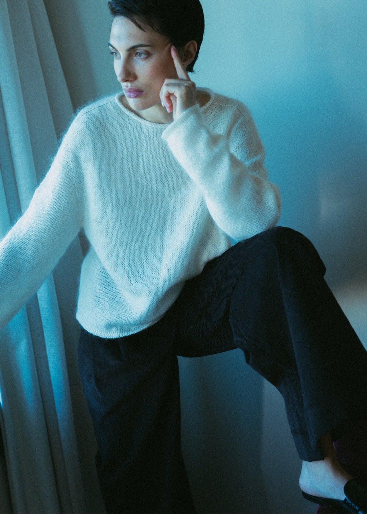 Person wearing a white sweater and dark pants sitting indoors.