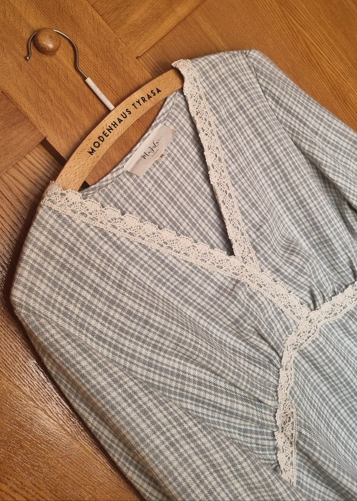 Gray checkered garment with lace trim on a hanger against a wooden floor background