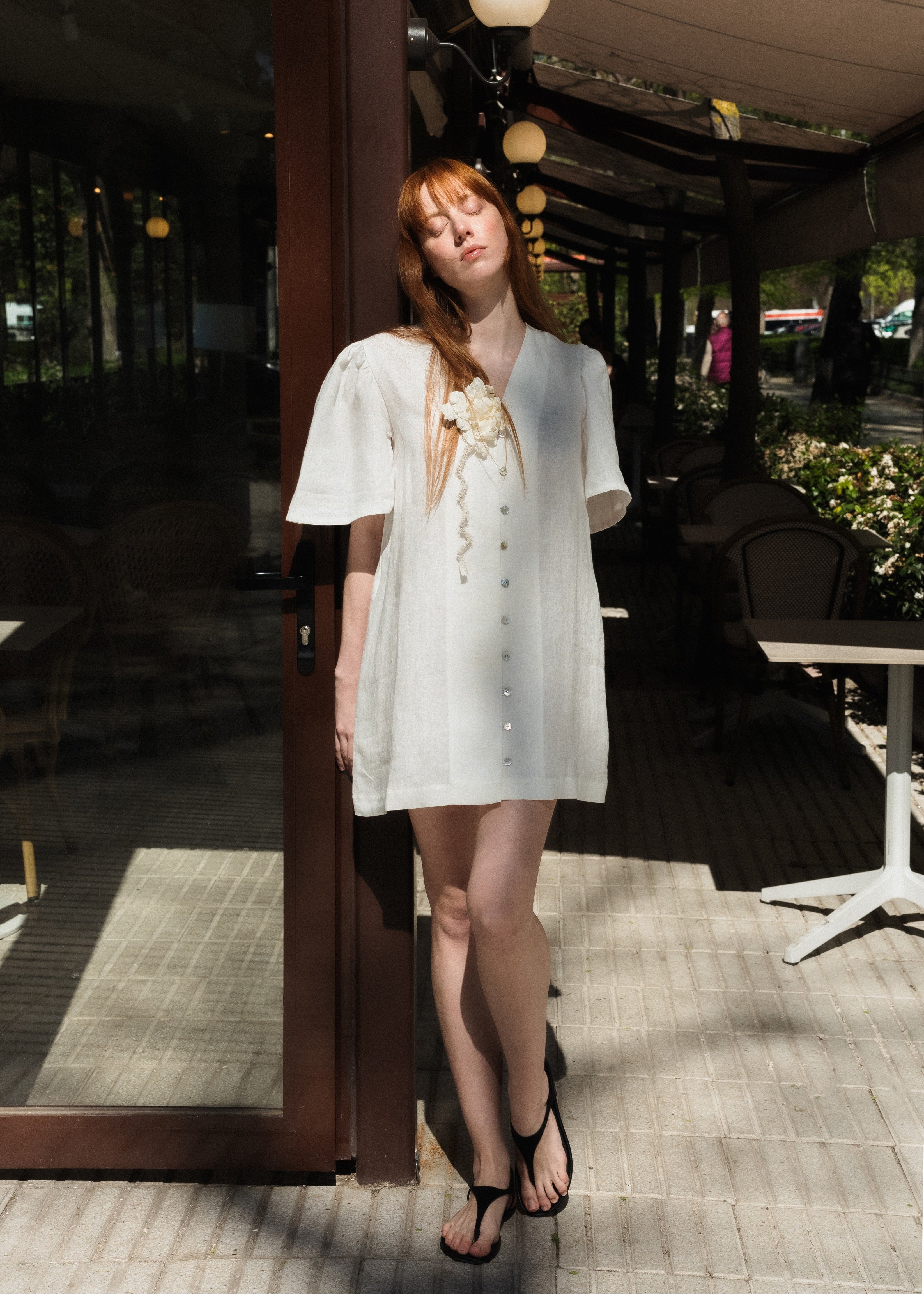 Woman in a white dress standing on a patio with outdoor furniture and decor.