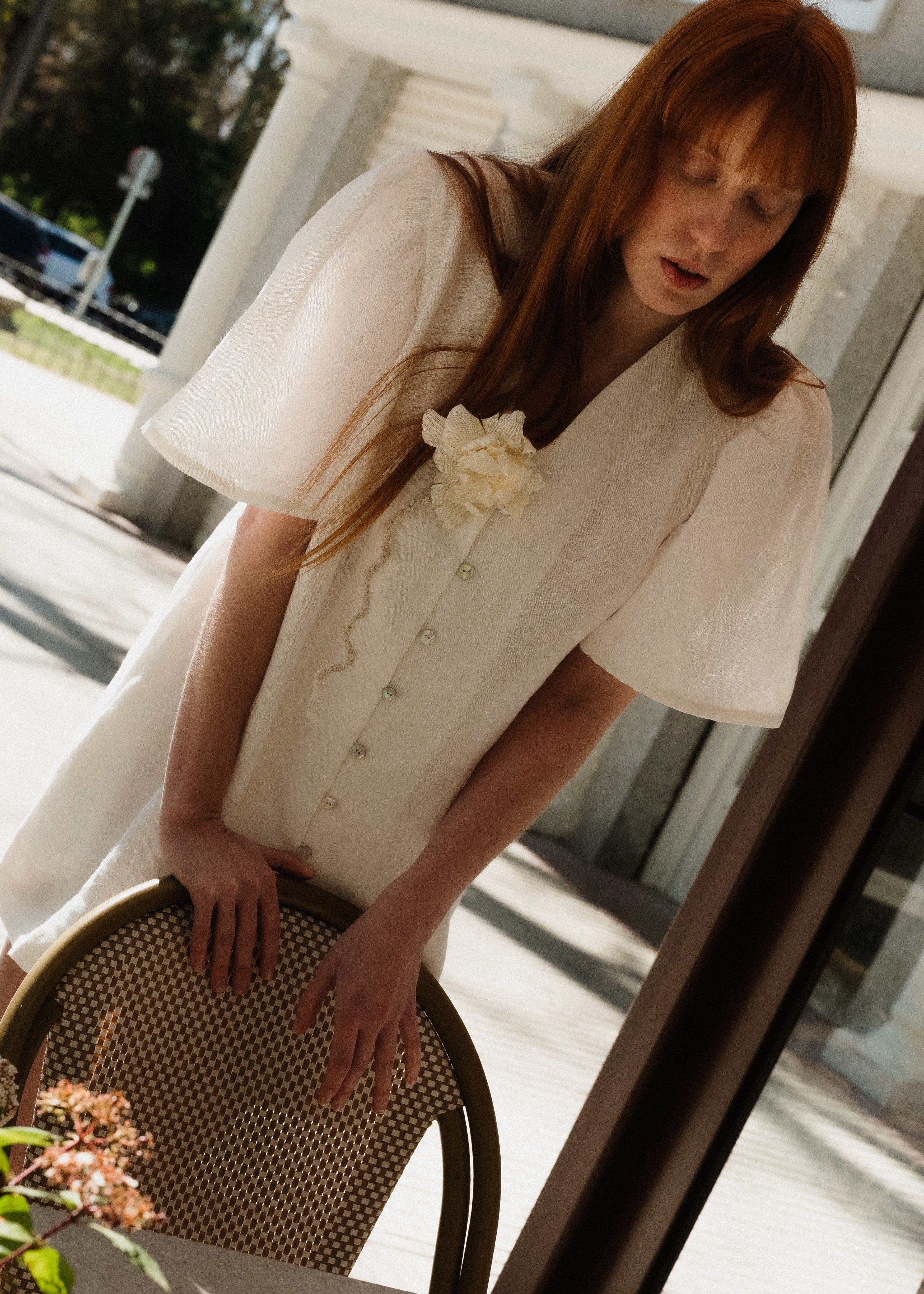 Woman in a white dress with a flower detail sitting on a chair outdoors.
