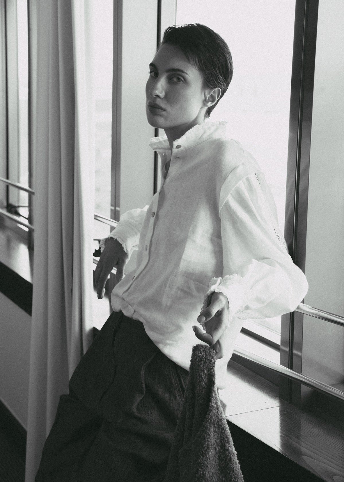 Person wearing a white shirt and dark pants in a room with large windows.