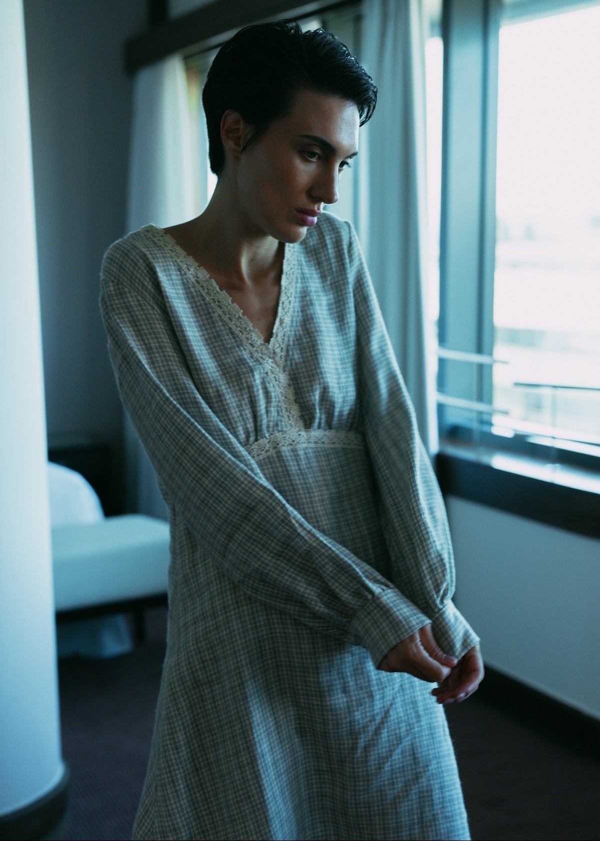 Woman in a checkered dress standing by a window in a room with neutral colors.